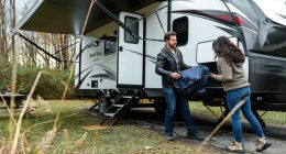 man in black jacket catching a bag in hand while a woman is unzipping the bag near a caravan