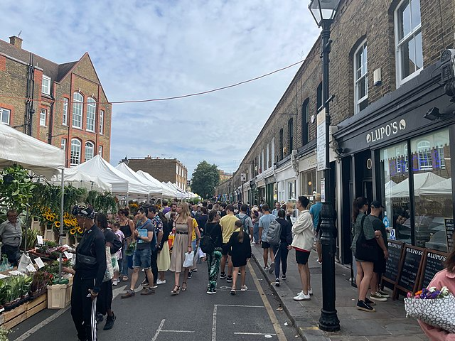 A bustling market scene with people walking along the street, engaging with vendors and exploring various stalls
