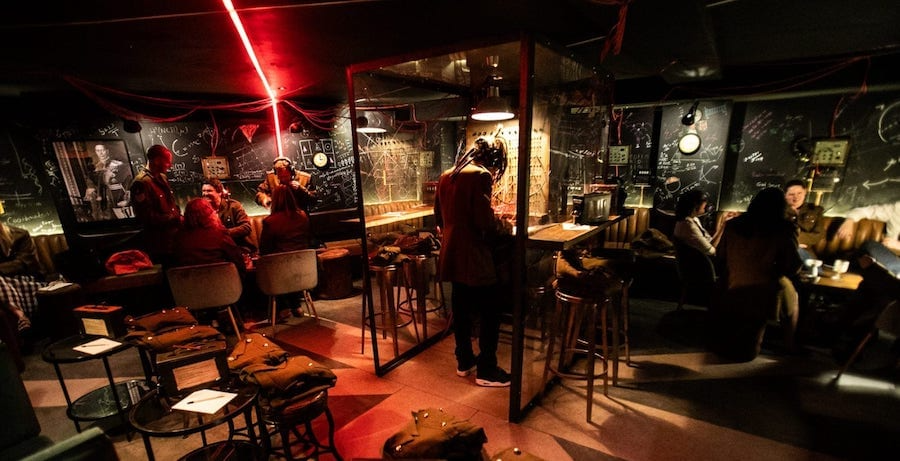 A lively bar scene featuring patrons seated at tables and stools, enjoying drinks and conversation in a vibrant atmosphere