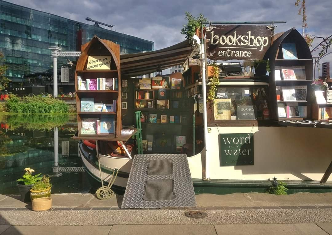 A boat filled with books rests peacefully along the edge of a tranquil canal